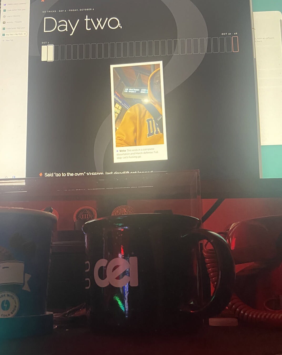 A desk at night: the Day two page on the monitor, a Wawa cold brew and a coffee mug below it.