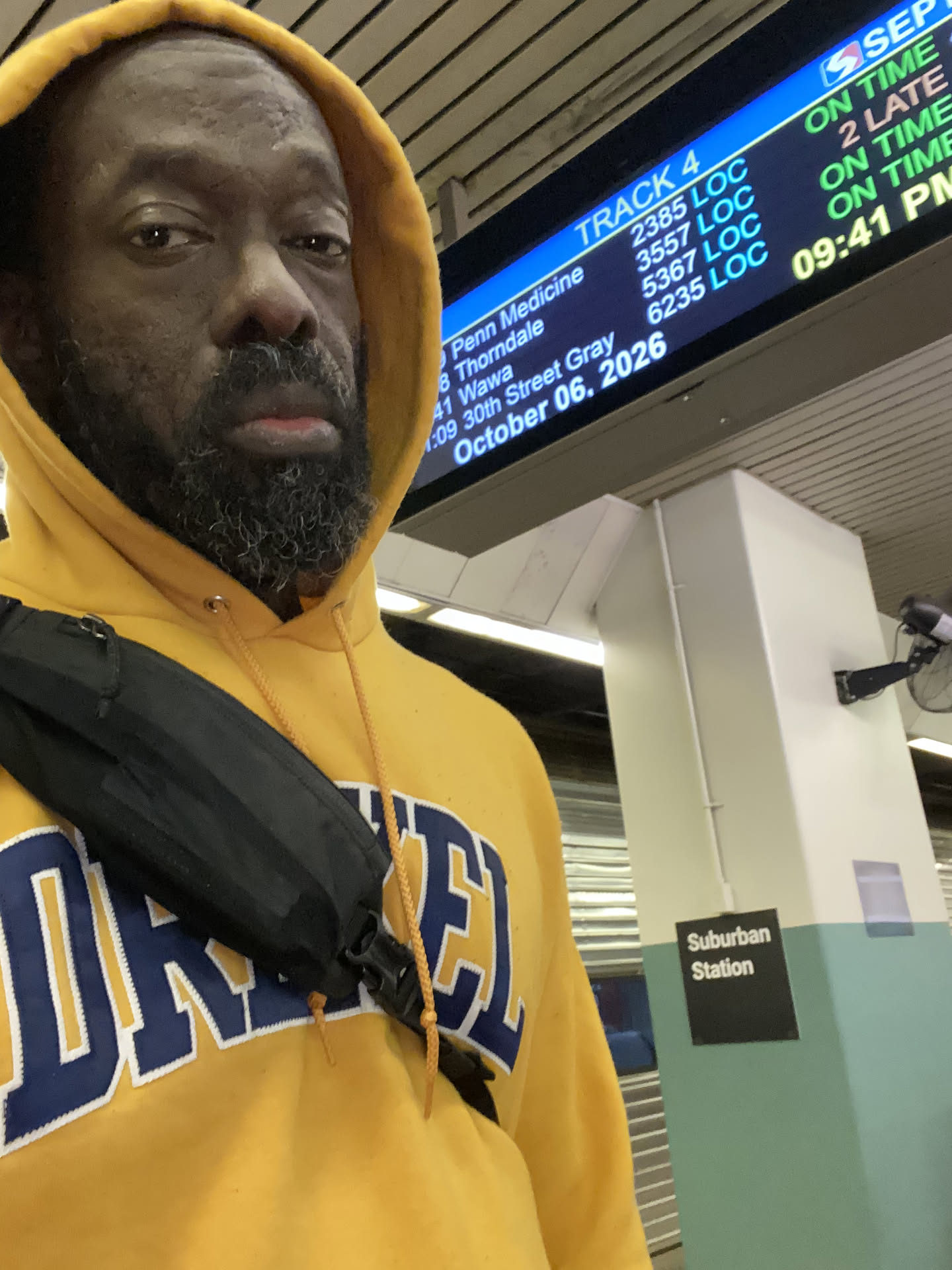 A selfie in a gold Drexel hoodie at Suburban Station, the departures board overhead reading 9:41 PM, October 6, 2026.
